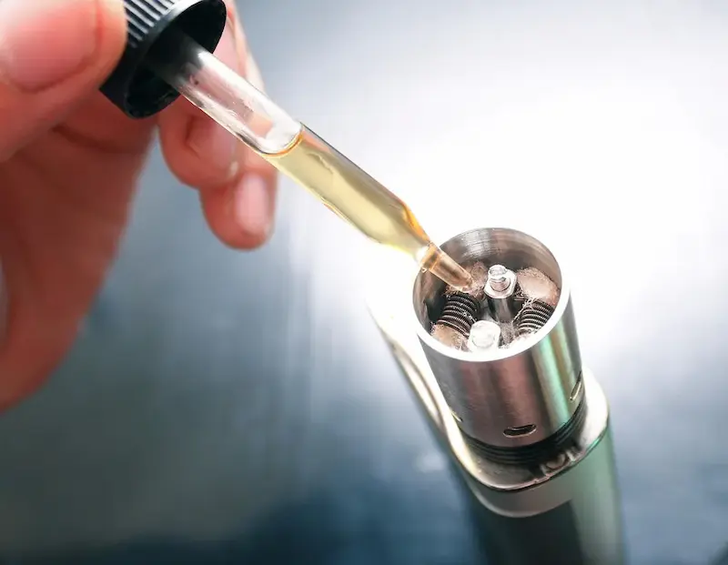 Golden e-liquid being dripped into a vape atomizer